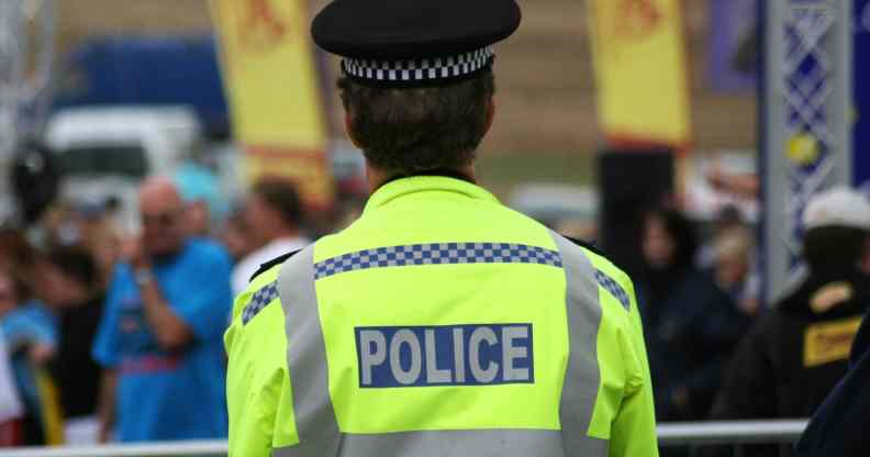 A police man wearing a reflective yellow jacket and police hat, his back turned to the camera