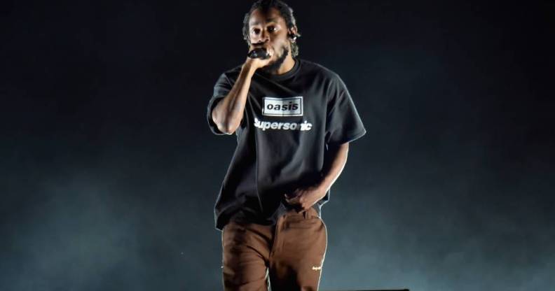 Kendrick Lamar raps on stage while wearing a black shirt and a brown pants