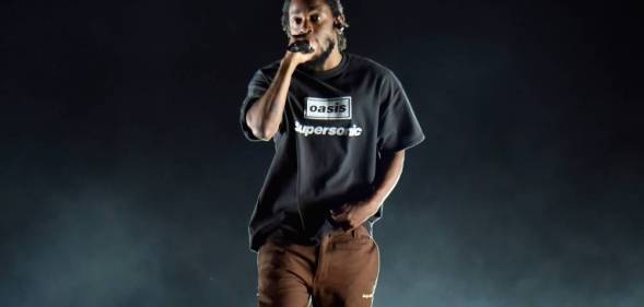 Kendrick Lamar raps on stage while wearing a black shirt and a brown pants