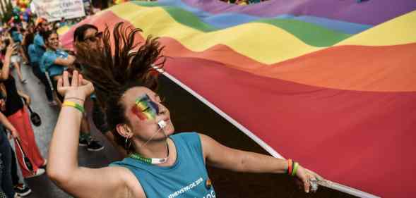 A participant dances while holding a large rainbow flag during the Athens Gay Pride