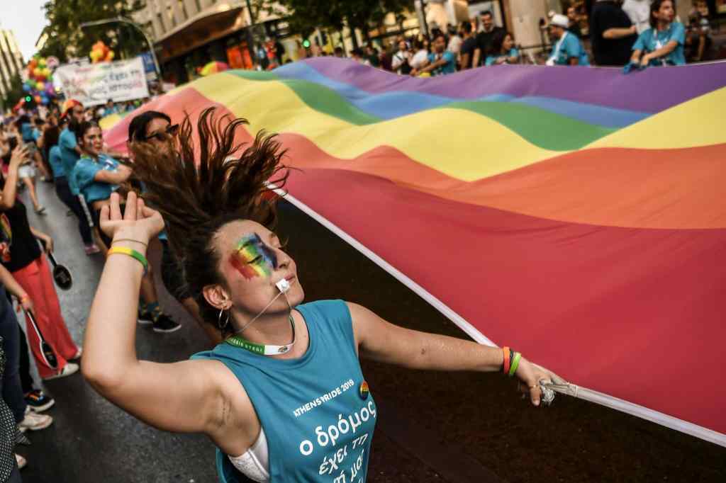 A participant dances while holding a large rainbow flag during the Athens Gay Pride