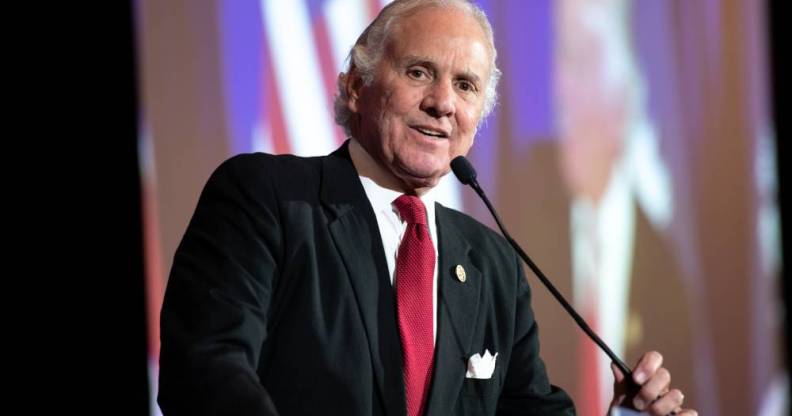 South Carolina governor Henry McMaster wears a white shirt, red tie and dark suit jacket as he speaks into a microphone on stage