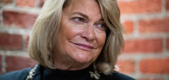 Senator Cynthia Lummis wears a dark outfit as she stares off camera with a brick wall in the background