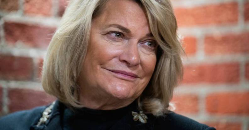 Senator Cynthia Lummis wears a dark outfit as she stares off camera with a brick wall in the background