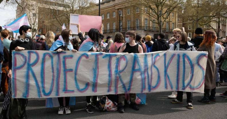 A group of people hold up a sign that reads 'protect trans kids' in blue and pink