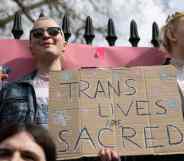 two people hold up a sign that reads 'trans lives are sacred'