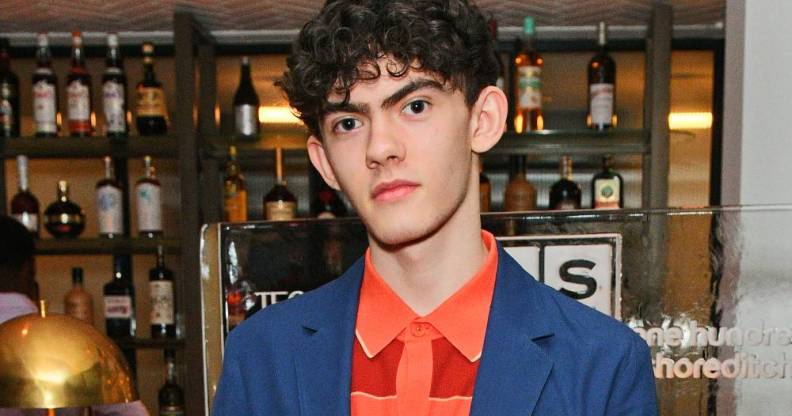 Heartstopper star Joe Locke stares at the camera while wearing an orange patterned shirt and blue jacket