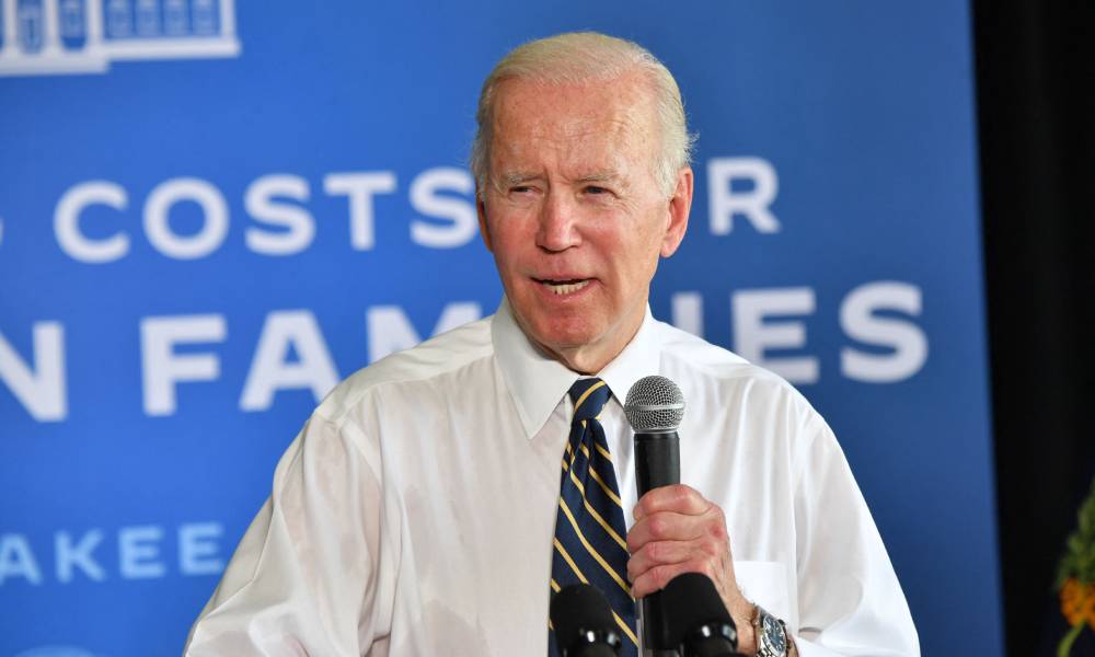 President Joe Biden speaks into a microphone while wearing a white button up shirt and a dark tie with stripes