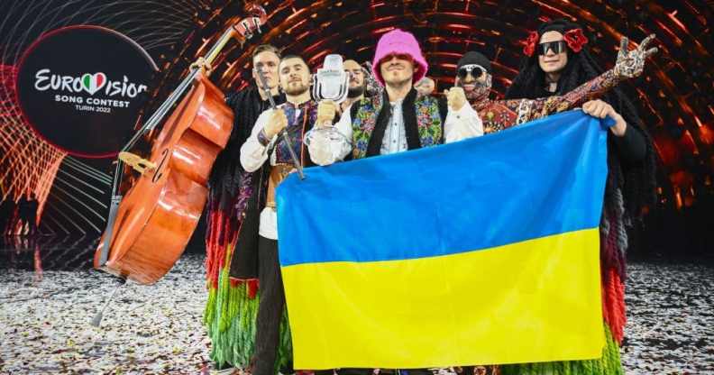 Eurovision winners Kalush Orchestra pose onstage with their trophy and Ukraine's flags