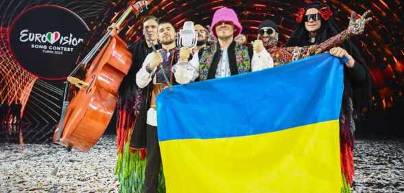 Eurovision winners Kalush Orchestra pose onstage with their trophy and Ukraine's flags