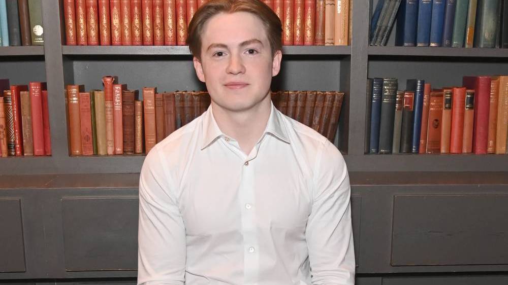 Kit Connor poses in the green room that appears to have books in it