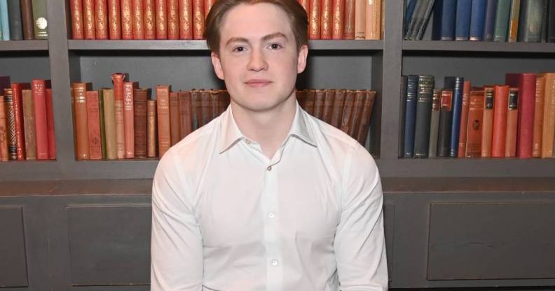Kit Connor poses in the green room that appears to have books in it