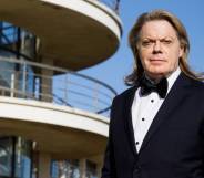 Eddie Izzard is see wearing a black suit jacket, white shirt and black bow tie