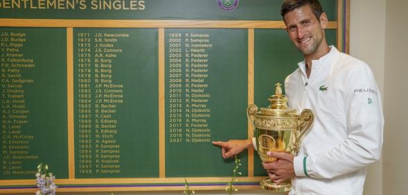 Novak Djokovic stands next to the Wimbledon men's honours board, which does not use titles