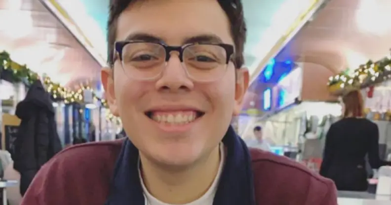 Julio Ramirez is seen smiling at the camera while wearing a black and red jacket with a white shirt and wearing black rimmed glasses