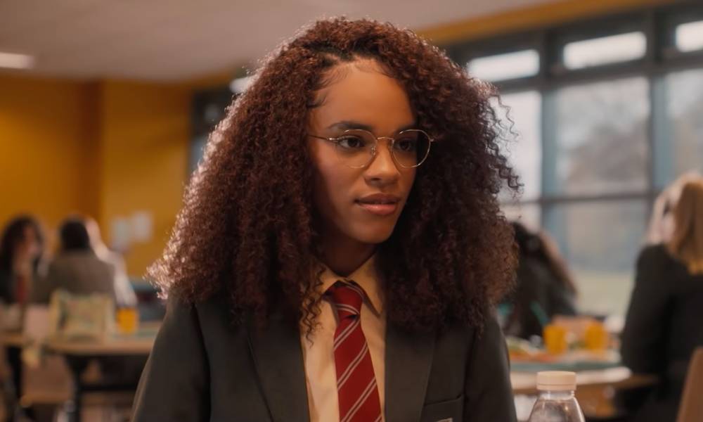 Yasmin Finney plays young teen Elle in Heartstopper. In this picture, the character is wearing a British school uniform with a dark jacket, white shirt and red striped tie