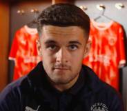 Blackpool football star Jake Daniels stares at the camera with football uniforms in the background