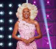 Drag Race icon RuPaul smiled at the camera while wearing a blonde wig and pink floral dress on the set of All Stars 7