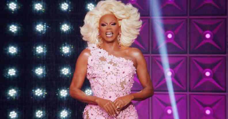 Drag Race icon RuPaul smiled at the camera while wearing a blonde wig and pink floral dress on the set of All Stars 7