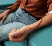 A person wearing a brown shirt with black polka dots and light blue jeans while donating blood