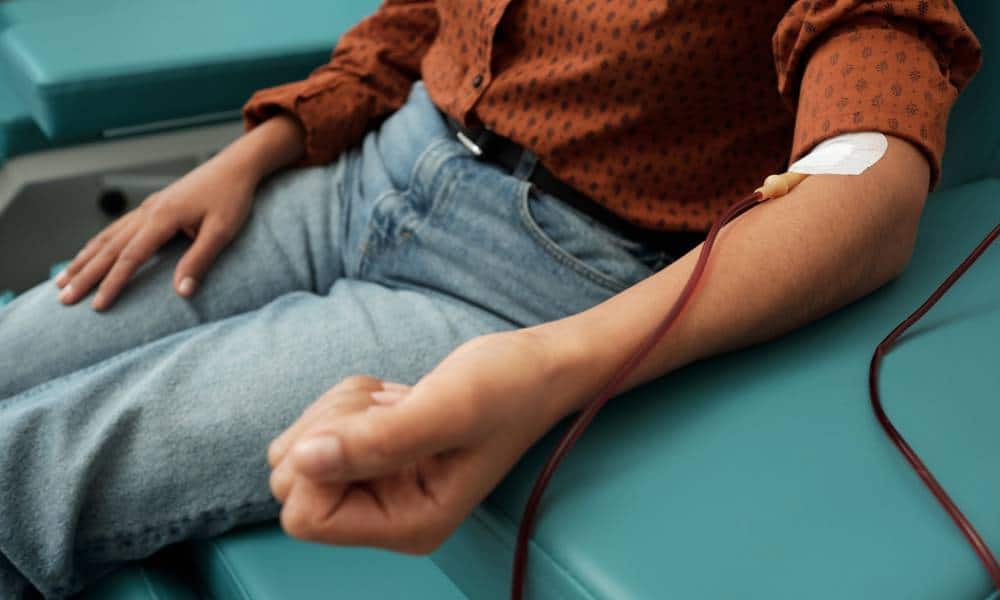 A person wearing a brown shirt with black polka dots and light blue jeans while donating blood