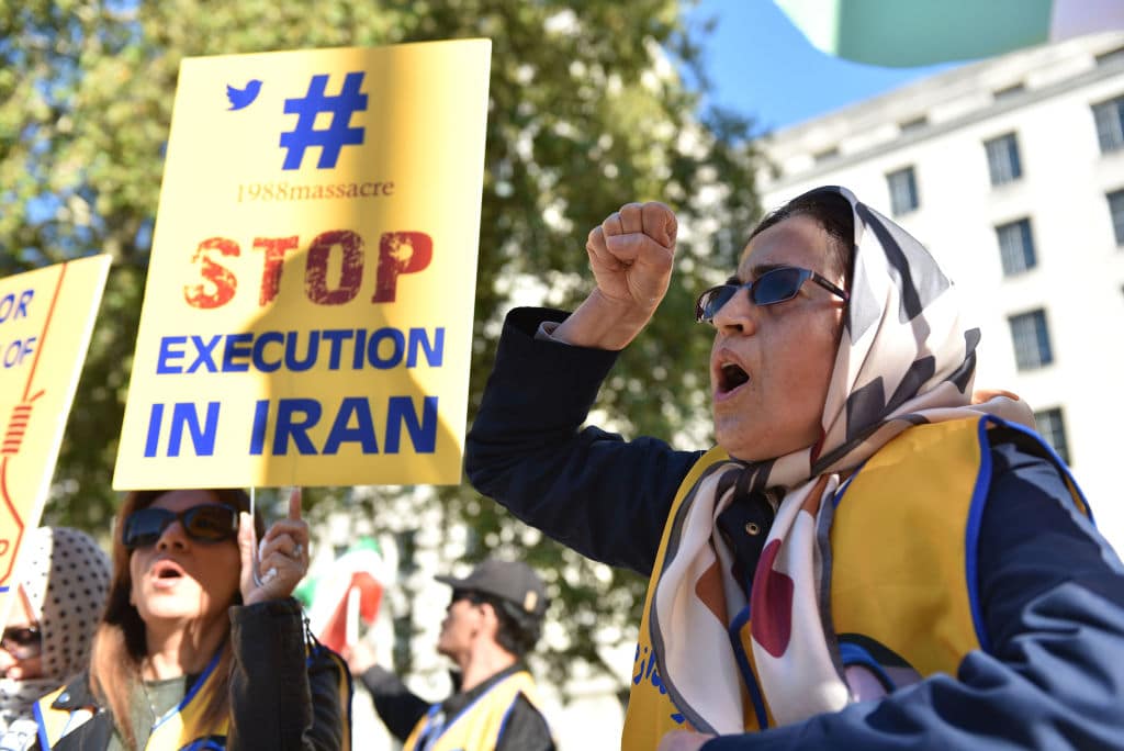 A woman shouting with her first in the air, a person next to her holds a placard that reads 'stop execution in Iran'