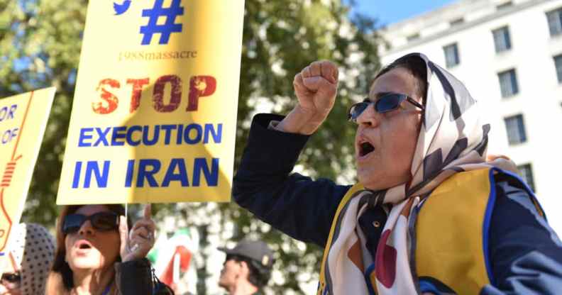 A woman shouting with her first in the air, a person next to her holds a placard that reads 'stop execution in Iran'