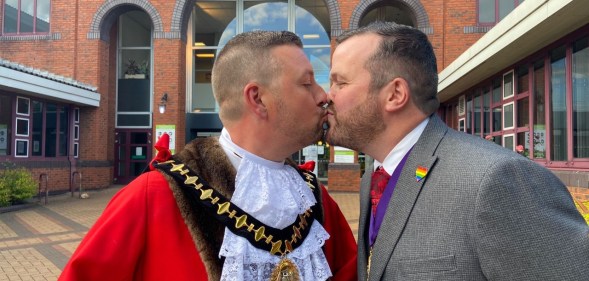 Richard Jones, in his red ceremonial mayor's cloak, kissing his partner, also named RIchard, who is wearing a grey suit