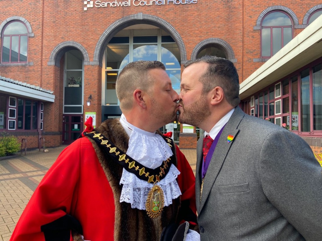 Richard Jones, in his red ceremonial mayor's cloak, kissing his partner, also named RIchard, who is wearing a grey suit