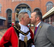 Richard Jones, in his red ceremonial mayor's cloak, kissing his partner, also named RIchard, who is wearing a grey suit
