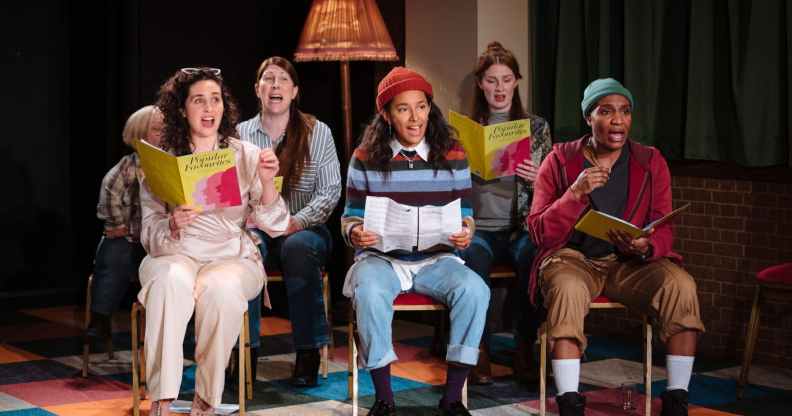 The cast of The Ministry of Lesbian Affairs sitting on chairs, holding songbooks and singing