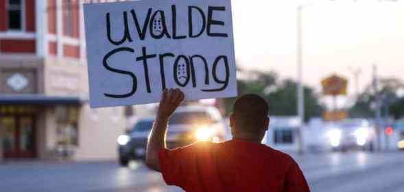 A person, with their back to the camera, holds a placard that says Uvalde strong