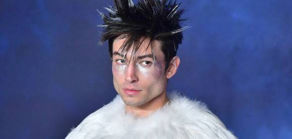 Ezra Miller wears a white fluffy top with their hair spiked up and wearing silver makeup on their face