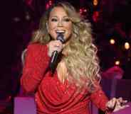 Mariah Carey sings into a microphone that she holds in one hand while wearing a red sparkly dress amid a festive Christmas set on tour