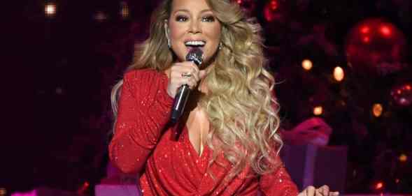 Mariah Carey sings into a microphone that she holds in one hand while wearing a red sparkly dress amid a festive Christmas set on tour