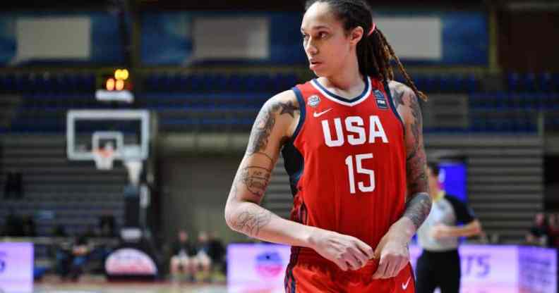 Brittney Griner wears a red basketball jersey with 'USA' and '15' written in white with blue panelling on the sides as she runs down a basketball court. Griner has her hair styled in locks and has multiple tattoos on both arms