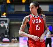 Brittney Griner wears a red basketball jersey with 'USA' and '15' written in white with blue panelling on the sides as she runs down a basketball court. Griner has her hair styled in locks and has multiple tattoos on both arms
