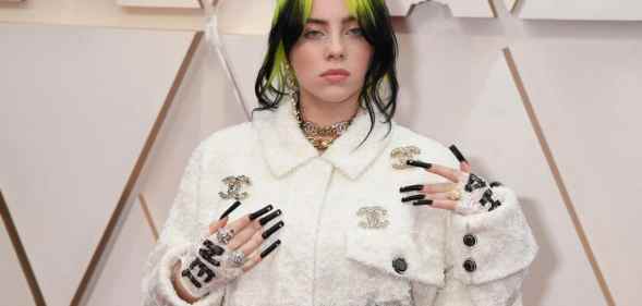 Singer Billie Eilish at Oscars 2020, wearing a white Gucci outfit, long black nails, and bright green and black hair.