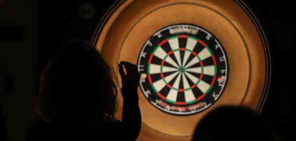 Silhouette of lady throwing darts at a dartboard