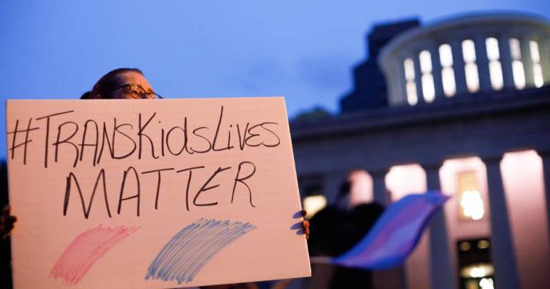 A transgender rights advocate holds a sign that reads '#TransKidsLives Matter' with pink and blue colours underneath as they outside the Ohio Statehouse during a rally against a trans sports ban bill