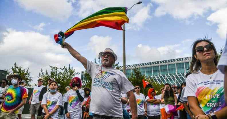 A person wearing a white shirt holds up a rainbow flag during a demonstration denouncing Florida's 'Don't Say Gay' law