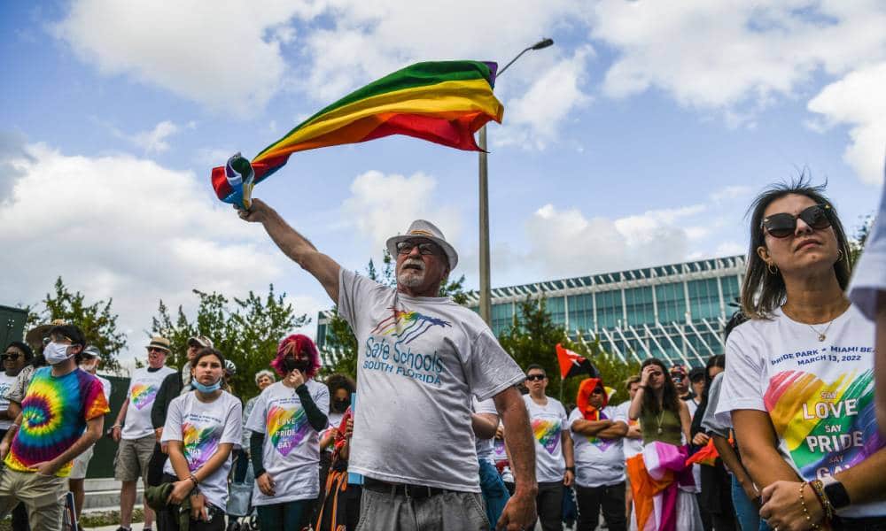 A person wearing a white shirt holds up a rainbow flag during a demonstration denouncing Florida's 'Don't Say Gay' law