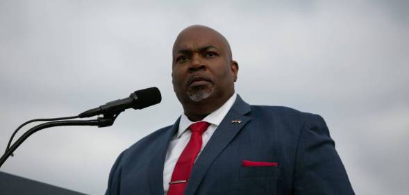 North Carolina lieutenant governor Mark Robinson stands at a podium while wearing a white button up shirt, red tie and blue suit jacket with a red pocket square