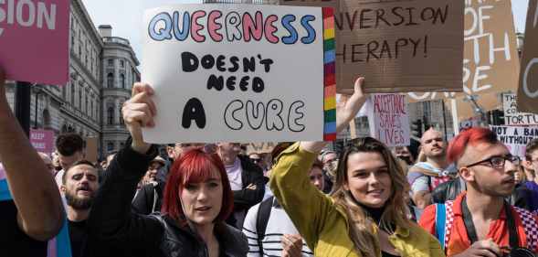 An anti-conversion therapy protester holds a sign that read "queerness doesn't need a cure"