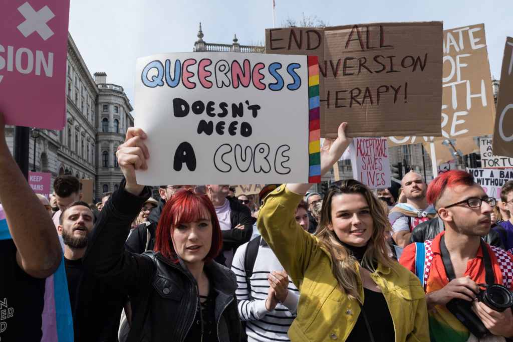 An anti-conversion therapy protester holds a sign that read "queerness doesn't need a cure"