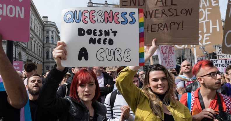 An anti-conversion therapy protester holds a sign that read "queerness doesn't need a cure"