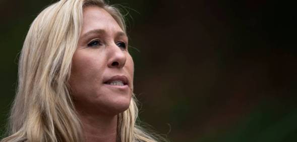 Marjorie Taylor Greene stares somewhere off camera while standing in front of a neutral coloured background