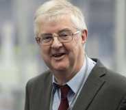 A photo shows first minister of Wales Mark Drakeford wearing a grey suit jacket, white shirt, red tie and glasses as he smiles at the camera
