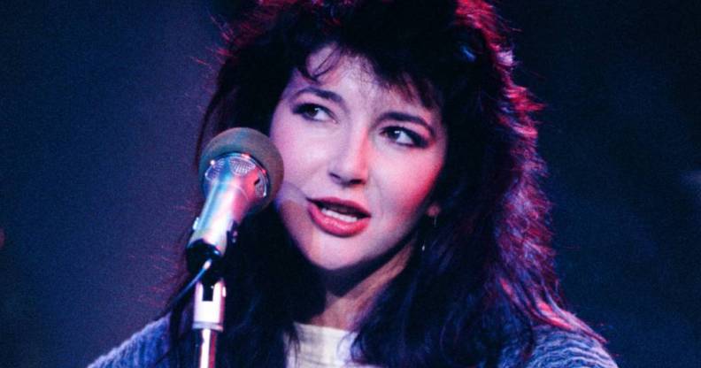 Kate Bush wears a white white shirt, long blue jumped as she sings into a microphone