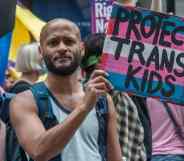 A person holds up a sign coloured in blue, pink and white like the trans Pride flag which reads 'Protect trans kids'